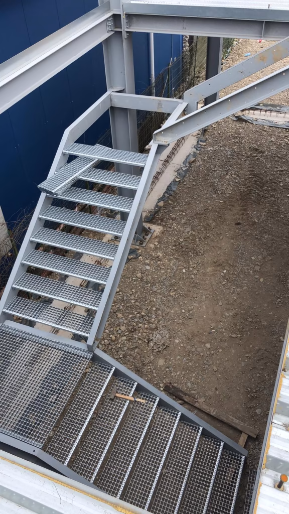 Montaj grătare metalice pe platformă industrială Montaj de grătare metalice galvanizate pe o platformă industrială; echipa respectă normele de siguranță.